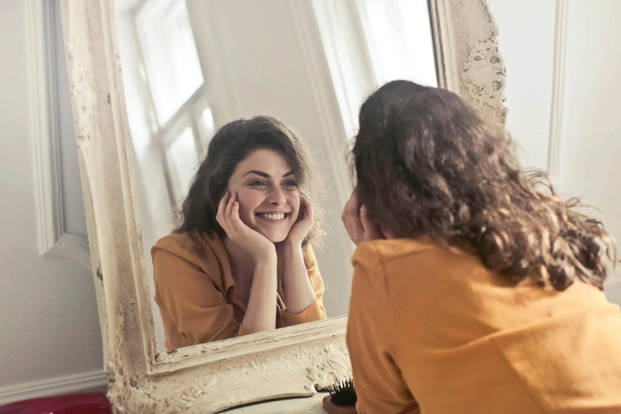 Woman in orange blouse smiling in a mirror